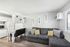 Modern living area with a stylish gray sectional, sleek kitchen space, and elegant feather artwork on the walls.