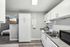 Modern kitchen with sleek white cabinetry, dual sink, and built-in stove; cozy bedroom glimpse with natural light and wood flooring.