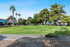 Expansive lush green lawn with tall palm and pine trees, featuring shaded picnic areas and vibrant community views.