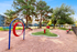 Charming outdoor playground featuring vibrant red and blue play equipment, surrounded by lush greenery and well-maintained communal spaces.