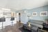 Modern living room with stylish open kitchen, featuring bar seating, cozy grey sofa, and vibrant artwork on pastel walls.