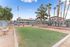 Inviting apartment complex with a serene outdoor area featuring a manicured green space, benches, and vibrant palm trees against a clear blue sky.