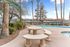 Inviting outdoor area featuring a sparkling pool, elegant stone seating, and lush landscaping with palm trees.