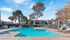 Inviting apartment complex with a sparkling swimming pool, spacious deck, and lush trees under a clear blue sky.