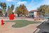 Vibrant playground with a charming red playhouse, lush green space, and a scenic backdrop of modern apartments, perfect for family living.