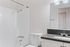 Bright and modern bathroom featuring a sleek white bathtub, elegant vanity with dark countertop, and stylish lighting fixtures.