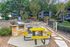 Charming outdoor area with vibrant yellow picnic table, BBQ grill, and lush surroundings, perfect for gatherings.