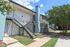 Charming apartment complex with modern exterior, featuring green landscaping and inviting staircases under a bright blue sky.