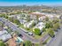 Aerial view of a charming apartment complex with lush greenery, modern white buildings, and ample parking, set against a vibrant urban skyline.