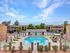Inviting apartment complex with a central swimming pool, surrounded by lush greenery and comfortable lounge chairs under a clear blue sky.