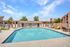 Inviting apartment complex with a sparkling outdoor pool, comfortable lounge chairs, and charming architectural details under a bright blue sky.
