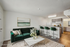 Chic and modern living room with plush green sofa, elegant marble coffee table, and sleek kitchen with bar stools, seamlessly merging style and comfort.