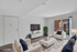 Bright and inviting living room with chic furnishings, large TV, and balcony access through sliding glass doors.