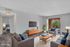 Bright and inviting living room with modern furniture, featuring cozy seating, a wooden coffee table, and a wall-mounted TV. Sliding glass doors open to a lush green view, enhancing the spacious atmosphere.