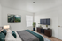 Bright and modern bedroom with tasteful decor, featuring a cozy bed with stylish pillows, a sleek TV mounted on the wall, and a dresser topped with elegant indoor plants.