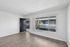 Bright and inviting apartment interior with large window, sleek wood flooring, and open entrance, perfect for modern living.