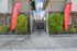 Inviting apartment entrance with lush greenery and vibrant 'Now Leasing' banners.