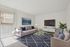 Bright, modern living room with chic furniture, large TV, and elegant decor, featuring a sunlit window and plush blue rug.