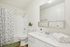 Bright and elegant bathroom featuring a spacious countertop with a large mirror, clean white fixtures, and a shower with a floral curtain.
