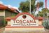 Charming Toscana Villas entrance with elegant signage surrounded by lush greenery and vibrant flags, showcasing a welcoming community atmosphere.