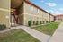 Charming apartment complex with a vibrant red roof, surrounded by lush greenery and a well-maintained walkway under a clear blue sky.