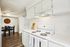 Bright, modern kitchen with sleek white cabinetry, electric stove, and cozy dining area featuring a stylish wooden wall clock.