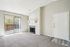 Bright and airy living room with plush carpet, cozy fireplace, and sliding glass doors leading to a private balcony.