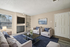 Virtually staged cozy living room with modern decor, plush seating, a large flat-screen TV, and abundant natural light streaming through the window.