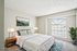 Bright and airy bedroom with a soft white color palette, featuring a cozy bed, elegant bedside lamps, and a large window letting in natural light, enhanced with virtual staging.