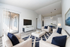 Bright and modern living room with stylish neutral furniture, a large flat-screen TV, and elegant decor. Features light wood flooring, sliding glass doors opening to a cozy balcony, and a chic dining area for seamless entertaining.