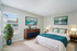 Elegant bedroom featuring a plush bed with teal accents, modern wooden furniture, and large window allowing abundant natural light.