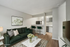 Elegant living area with plush dark green sofa, chic artwork, and an open-plan kitchen featuring sleek bar stools, perfect for modern living.