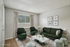 Sleek and cozy living room with plush dark green seating, elegant marble-top coffee table, and tasteful wall art, set against a backdrop of soft beige walls and abundant natural light.