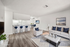 Contemporary open-plan living room with stylish white furnishings, elegant accent pillows, and a sleek kitchen with a breakfast bar and modern stools, creating a welcoming and chic atmosphere.