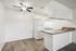 Bright kitchen with modern ceiling fan, sleek white cabinets, and spacious countertop in a cozy apartment.