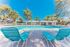 Inviting outdoor pool surrounded by lush palm trees, featuring stylish lounge chairs for relaxation under a clear blue sky.