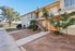 Charming apartment building with vibrant orange accents, lush greenery, and a welcoming staircase in a serene, sunny neighborhood.