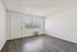 Bright and airy living area with modern laminate flooring, large window with vertical blinds, and sleek white walls.