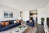 Modern living room with sleek blue seating, accent pillows, and a vibrant wall art, seamlessly connected to a contemporary kitchen. Bright and inviting space accented by a floor plant and stylish decor, ideal for relaxation and entertainment.