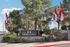 Inviting entrance to Harmon Hills with vibrant red and white flags surrounded by lush greenery and tall trees, offering a serene living environment.
