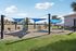 Inviting outdoor fitness area with modern exercise equipment and vibrant shade sails on a sunny day, perfect for a refreshing workout amidst serene surroundings.