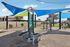 Inviting outdoor fitness area with modern exercise equipment under vibrant blue and green sunshades, perfect for active lifestyles.