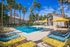 Vibrant outdoor pool area with colorful lounge chairs and yellow umbrellas, surrounded by tall palm trees under a clear blue sky, perfect for relaxation.