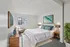 Inviting bedroom with stylish decor, featuring a plush white bed, elegant side tables, and vibrant artwork, complemented by natural lighting from a large window.