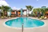 Inviting apartment complex with a sparkling blue pool, surrounded by vibrant palm trees and modern architecture.