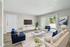 Bright and modern living room with elegant decor, featuring a sleek white sofa, plush navy chairs, and a glass-top coffee table. Large sliding doors open to a lush outdoor view, enhancing the room's welcoming atmosphere.