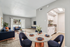Chic, virtually staged living area with plush navy seating, elegant dining setup, and modern kitchen nook, leading to a bright patio through large glass doors.