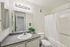 Sleek and modern bathroom featuring a spacious vanity with a large mirror, elegant lighting, and a convenient shower-tub combo accented by a fresh plant.