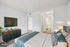 Modern bedroom with chic decor, featuring a mounted TV, stylish dresser, and elegant bed with plush pillows in a bright, airy space.