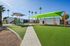 Vibrant playground with slides and tall palm trees under sunlit blue skies, surrounded by modern apartment buildings.